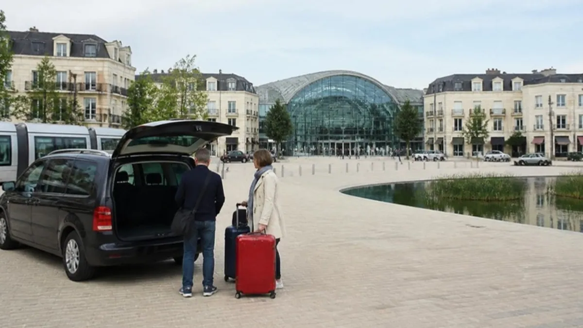 Shopping district plaza with a glass-roofed centre, a lake and a minivan dropping off travellers